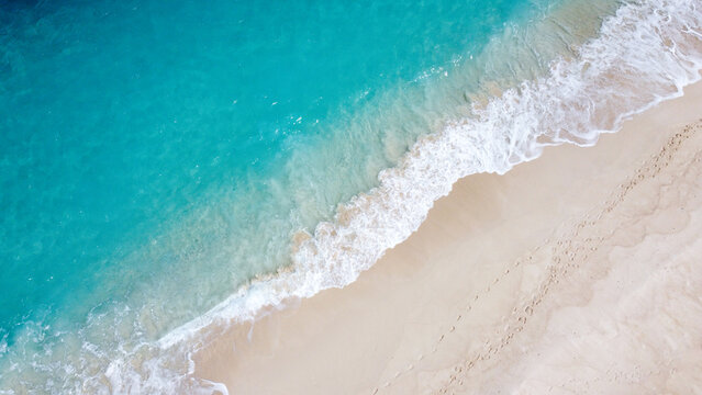 Aerial birdseye view of white frothy waves breaking on sandy beach with crystal clear tropical ocean water in tropical island paradise