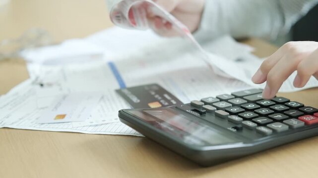Person calculating monthly household bills with receipts, invoices, credit cards and a calculator for debt management and family expense planning.