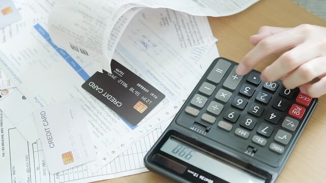 Hand pressing a calculator while reviewing monthly bills, receipts and credit card expenses for household budget planning and debt management.