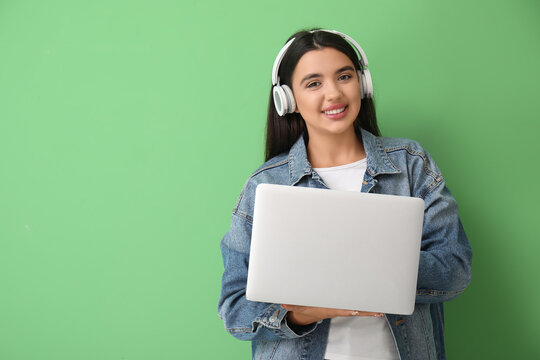 Happy young female programmer in headphones with laptop on green background