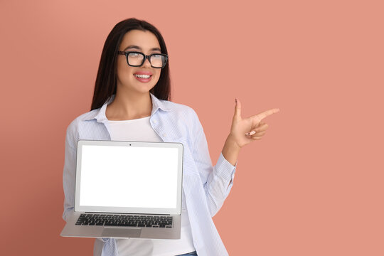 Young female programmer with laptop pointing at something on orange background