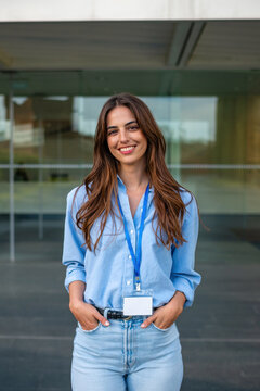 Smiling young businesswoman with ID badge standing outside office