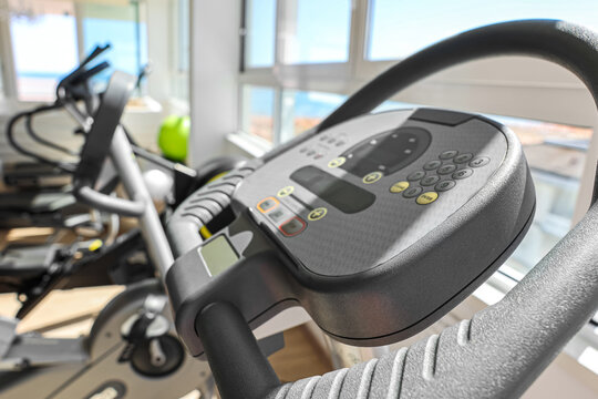 Modern gym elliptical machine console with digital display and control buttons for fitness training, the exercise equipment is ready for a workout session in a bright gym setting with natural