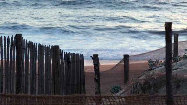 Static shot of calm ocean waves crashing on the beach shore behind a wooden fence at Labenne-Ocean, Landes, France