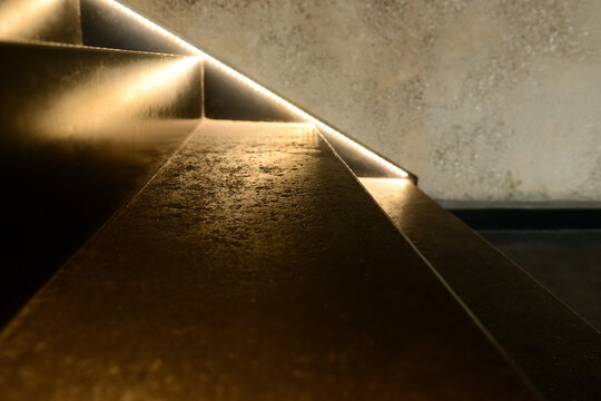 Modern architectural staircase with warm LED strip lighting and textured concrete steps, contemporary interior design element