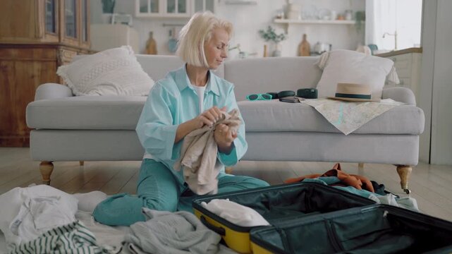 Aged woman packing clothes in suitcase, planning summer vacation, traveling. Single lady preparing to weekend trip in summertime, carefree female traveler enjoying future holidays, vertical shot