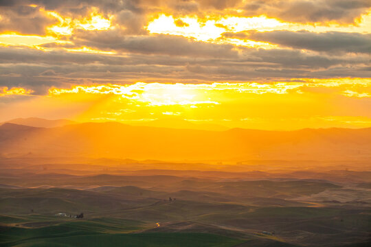 Golden sunbeams stream over rolling green hills