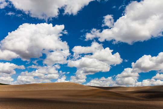 Big white clouds drift over rolling brown farm hills