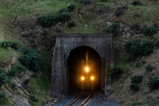 Train with bright headlights emerges from dark mountain tunnel