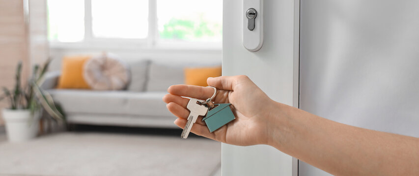 Female hand with key from house near open door in room, closeup