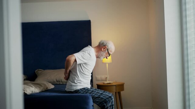 Senior man with backache sitting on bed.
