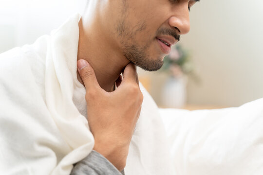 Sick male feeling painful with throat swallowing difficulty, touching his neck with blanket on shoulders, healthcare symptom concept.