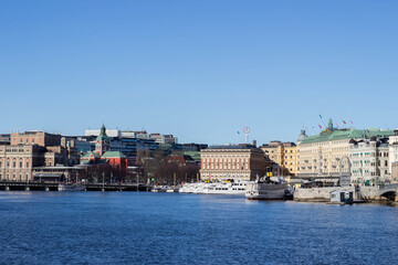 Fototapeta premium Scenic view of Stockholm waterfront featuring historic buildings, boats, and clear blue sky, showcasing the architectural beauty of Sweden's capital city