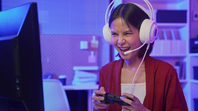Excited young Asian girl playing video game with headset and joy stick controller at home