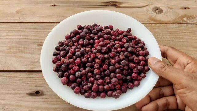 Closeup of hand placing ceramic plate full of fresh falsa berries on old wooden table for summer healthy snack