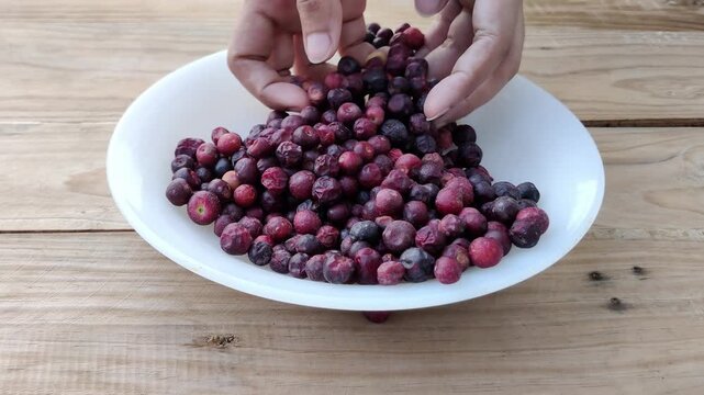 Hand mixing fresh phalsa berries in white plate on rustic table