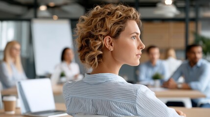 Fototapeta premium Woman with curly hair listens during a meeting in a modern office space with coworkers present