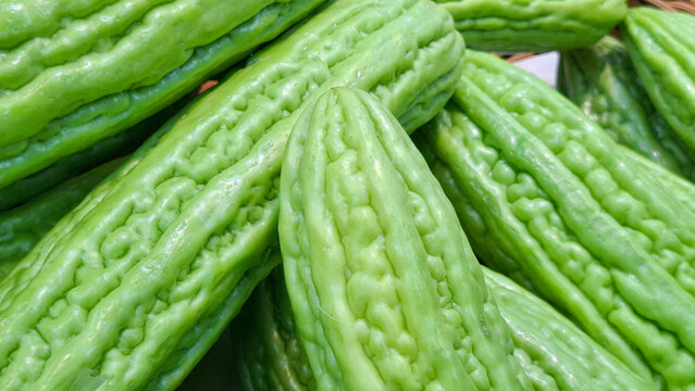 Fresh organic bitter melon gourds with textured bumpy skin stacked together at a local asian grocery market