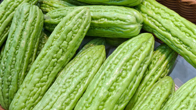 Group of ripe bumpy bitter melon gourds neatly arranged in a wooden crate basket at a traditional asian street market