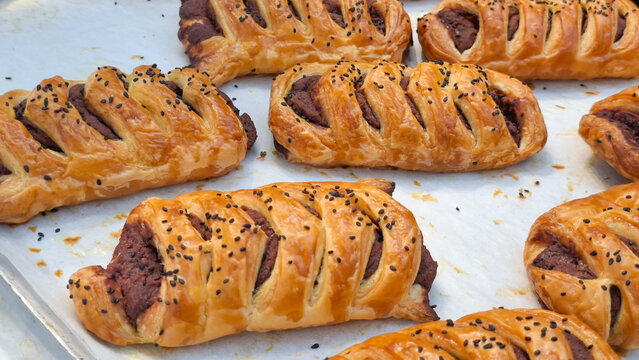 Freshly baked flaky braided puff pastry filled with sweet delicious paste filling and sprinkled with roasted sesame seeds on baking sheet