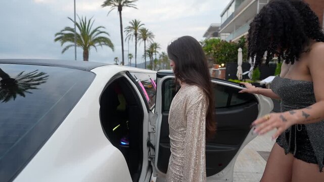 Group of fashionable young women in elegant dresses getting into a luxurious white limousine for a glamorous night out, enjoying a bachelorette party or special event in a coastal city