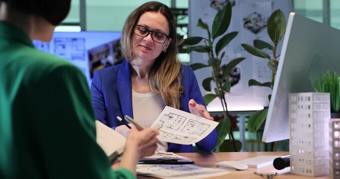 Designer shows technical sketches of apartments. Woman presents building designs and discusses construction possibilities with client. Slow motion