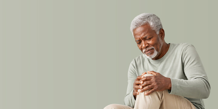 Painful senior man holding knee. Older black man suffering from joint pain or arthritis. Health concept for geriatric care. banner format