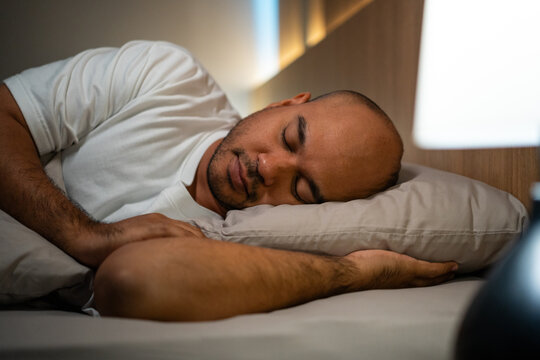 Young man lying in the bed at night. Man sleeping well in comfortable cozy fresh bed on soft pillow linen. Health and rest concept.