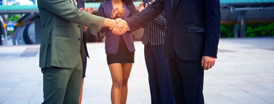 The celebrating business success and achievement with a handshake and deal agreement between two business partners with team clapping
