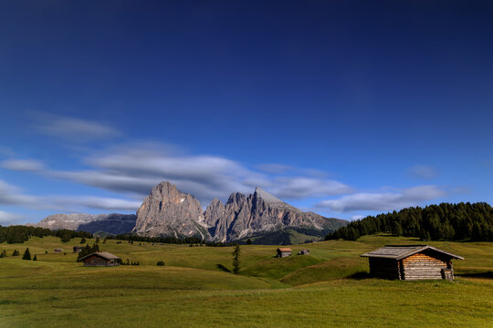 View over the alpine meadows with mountain cabins towards the Langkofel group with the peaks of Langkofel and Plattkofel on the Seiser Alm, Dolomites, South Tyrol, Italy.