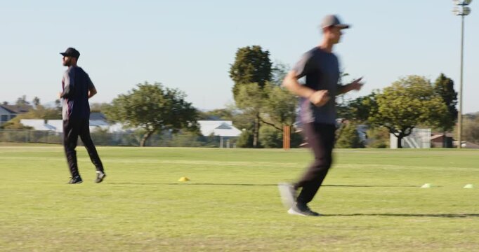 Diverse male team, coach holding yellow disc starting running drills across cones on field