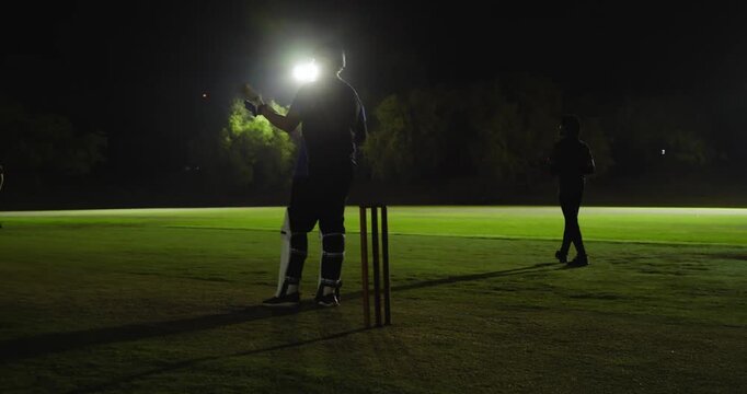 Diverse male cricketers reacting to bowler delivery training defending and catching, floodlights
