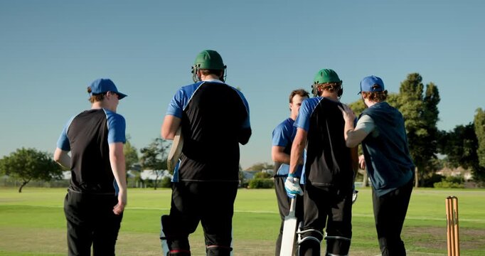 Five male cricket players strapping gear, entering pitch, tapping crease line for next over