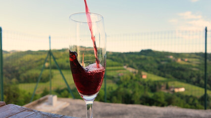 Obraz premium Red Wine Pouring into a Glass with Scenic Vineyard Valley Background