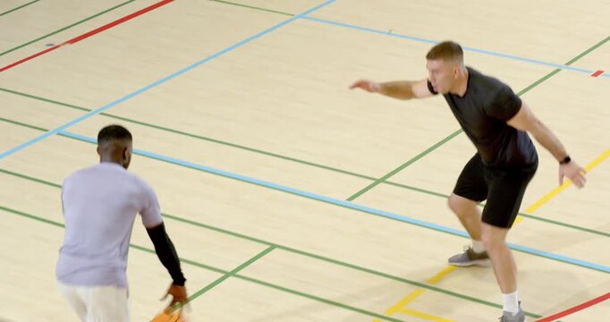 Diverse male friends practicing on court, bouncing, shooting orange basketball, stealing,