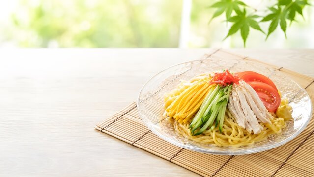 夏の冷やし中華 涼しげなガラス皿に盛った冷たい中華麺 彩り野菜 緑の背景 コピースペース付き