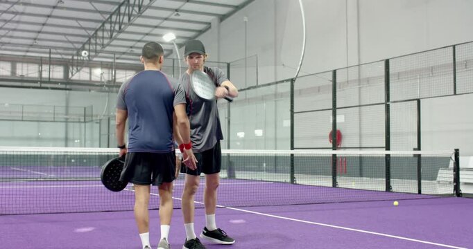 Forehand shot ending rally prompts diverse male doubles teams shaking paddles, hugging at net