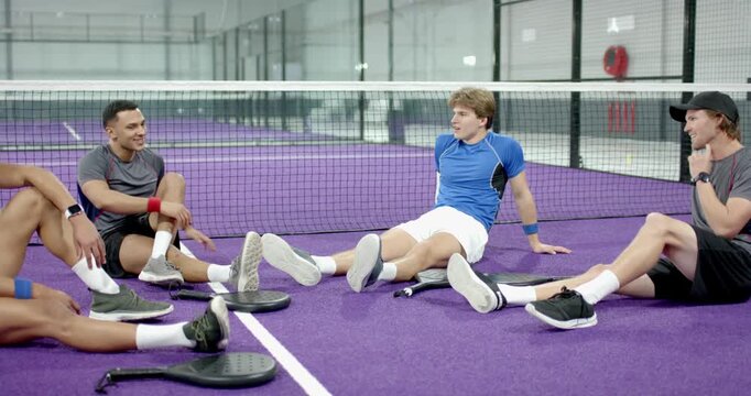 Male player rocking legs then stretching hamstrings on court with padel rackets