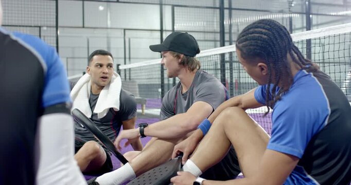 Diverse male friends following tip from player pointing paddle, showing swing on purple padel court