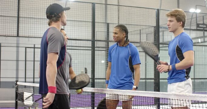 Diverse male players bumping elbows post match, shaking hands, tapping paddles on purple court