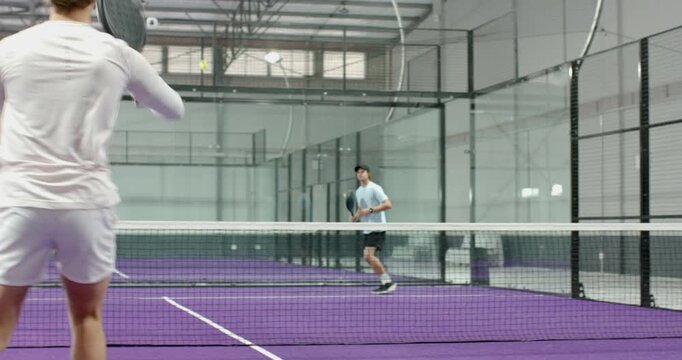 Male padel player on purple court serving, volleying, lobbing, retrieving ball, signaling end