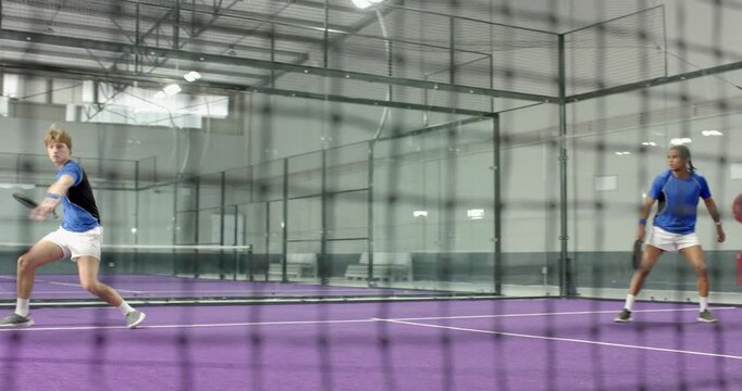 Diverse male teammates rallying on fed ball, retrieving balls, resetting on padel court