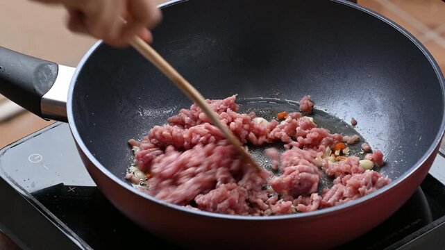 Hand using wooden spatula to stir-fry minced pork with garlic and chili inside a pan, Cooking Thai food