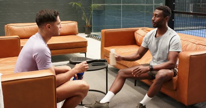 Diverse male friends passing bottle, fist bumping planning match in sports lounge