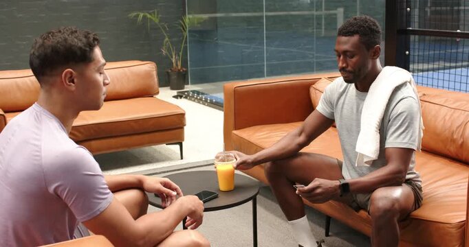 Post-workout two men taking phones sipping juice shaking hands parting in gym lounge