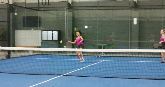 Female padel opponents reacting to lobbed ball, hitting volley to sustain rally on court