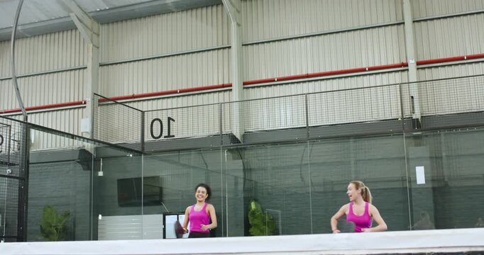 Diverse females in pink tops responding to ball tracking volley on padel court shaking hands