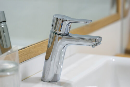 modern bathroom sink with a chrome faucet on a light wood countertop in front of a white tiled wall and mirror