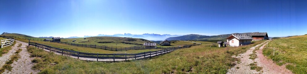 Panoramic view of the Dolomites mountain range with rustic alpine huts and grassy pastures in summer, South Tyrol, Italy © vlocka