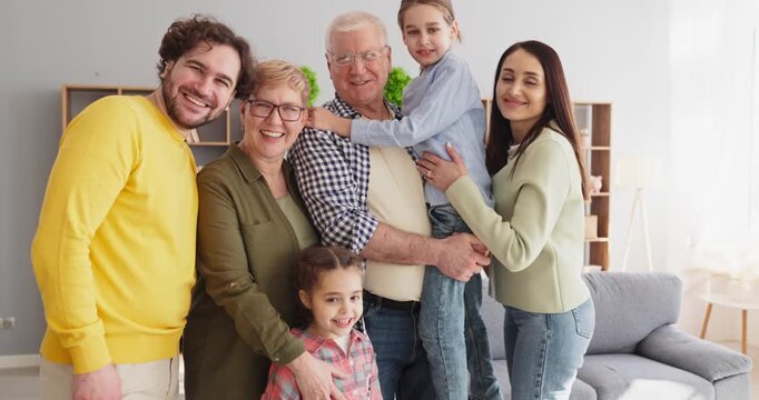 Family grandparents parents and children hugging together. Warm indoor scene of a joyful group embracing at home in a cozy room, smiling and united. Theme of love and generational connection.